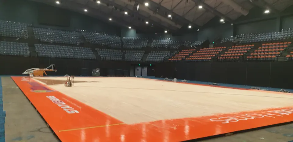 Indoor basketball arena with a partially refinished timber court and bright orange perimeter