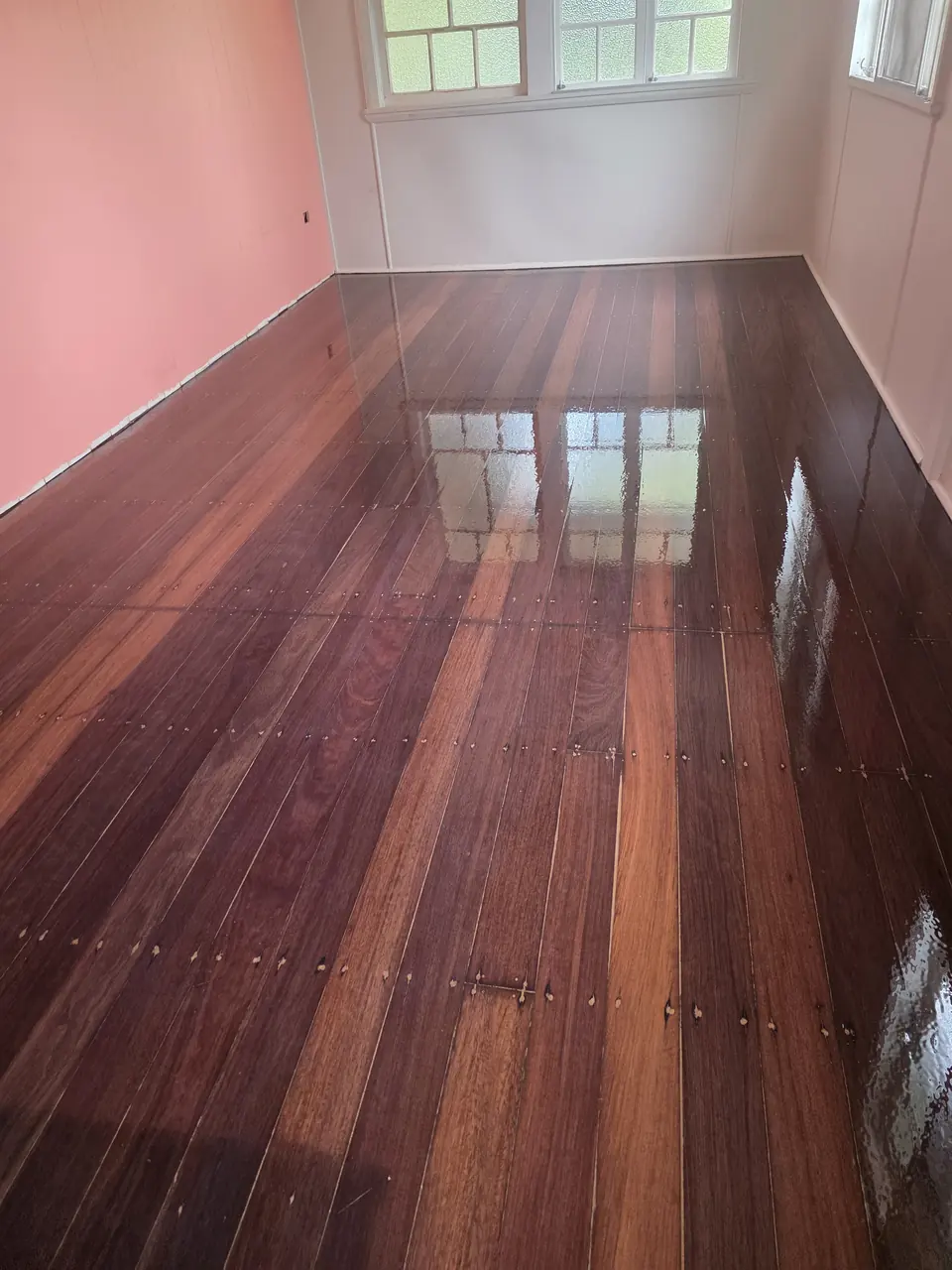 Glossy reddish timber boards extending across a room with pale pink walls